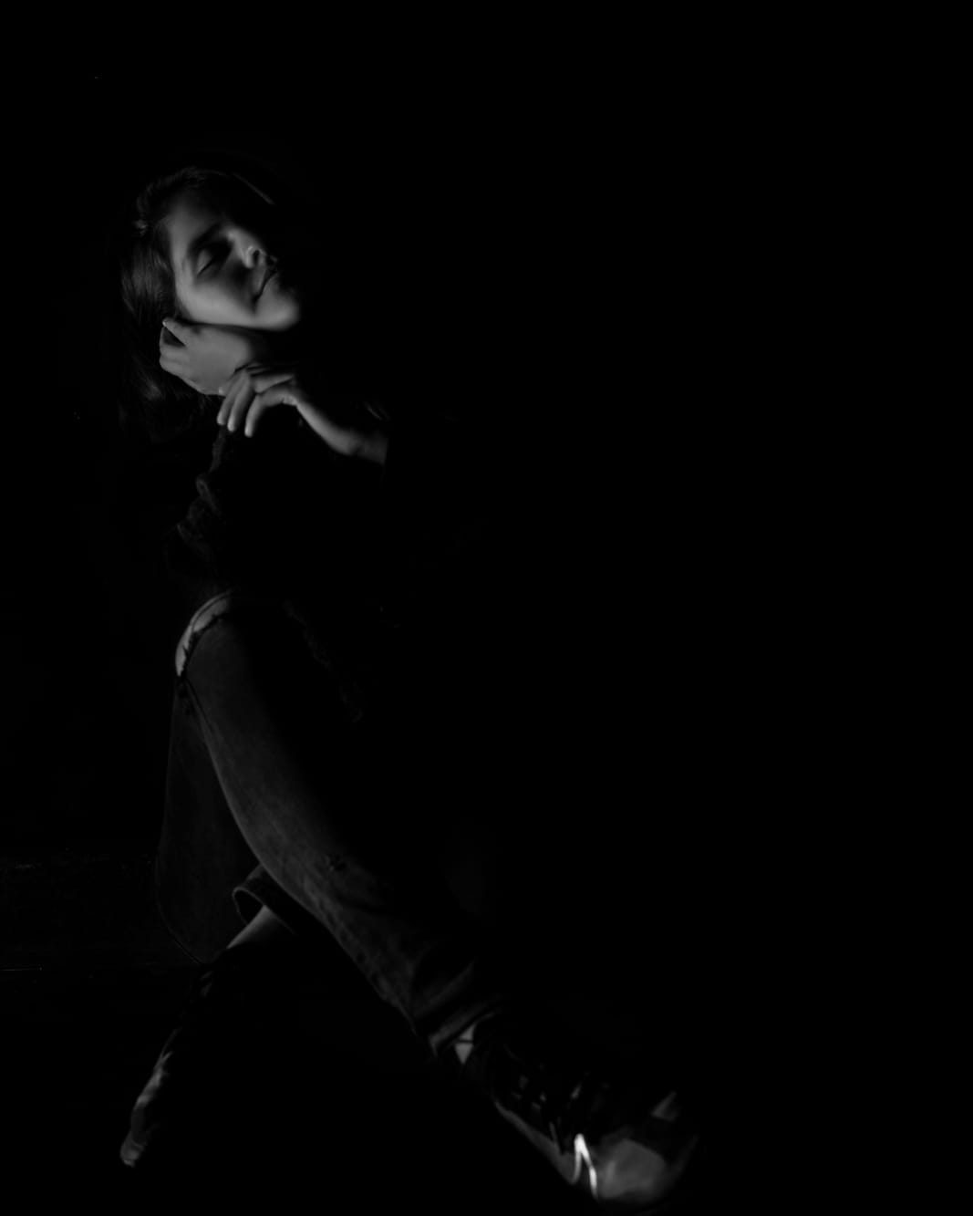 A dancer lit by a single hard light against near-total darkness.