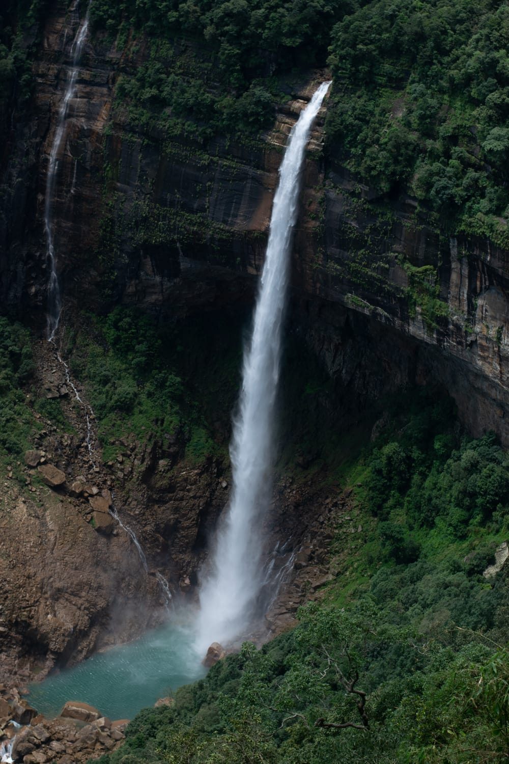 Nohkalikai Falls dropping down a green cliff face into a turquoise pool.