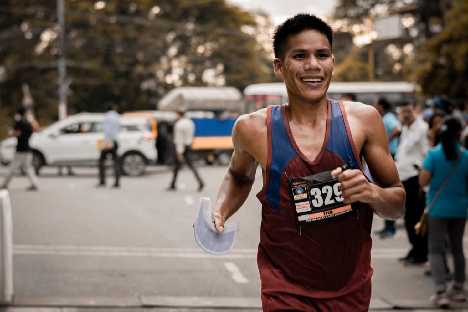 A marathon runner grinning mid-stride on a city street, race bib pinned to his vest.